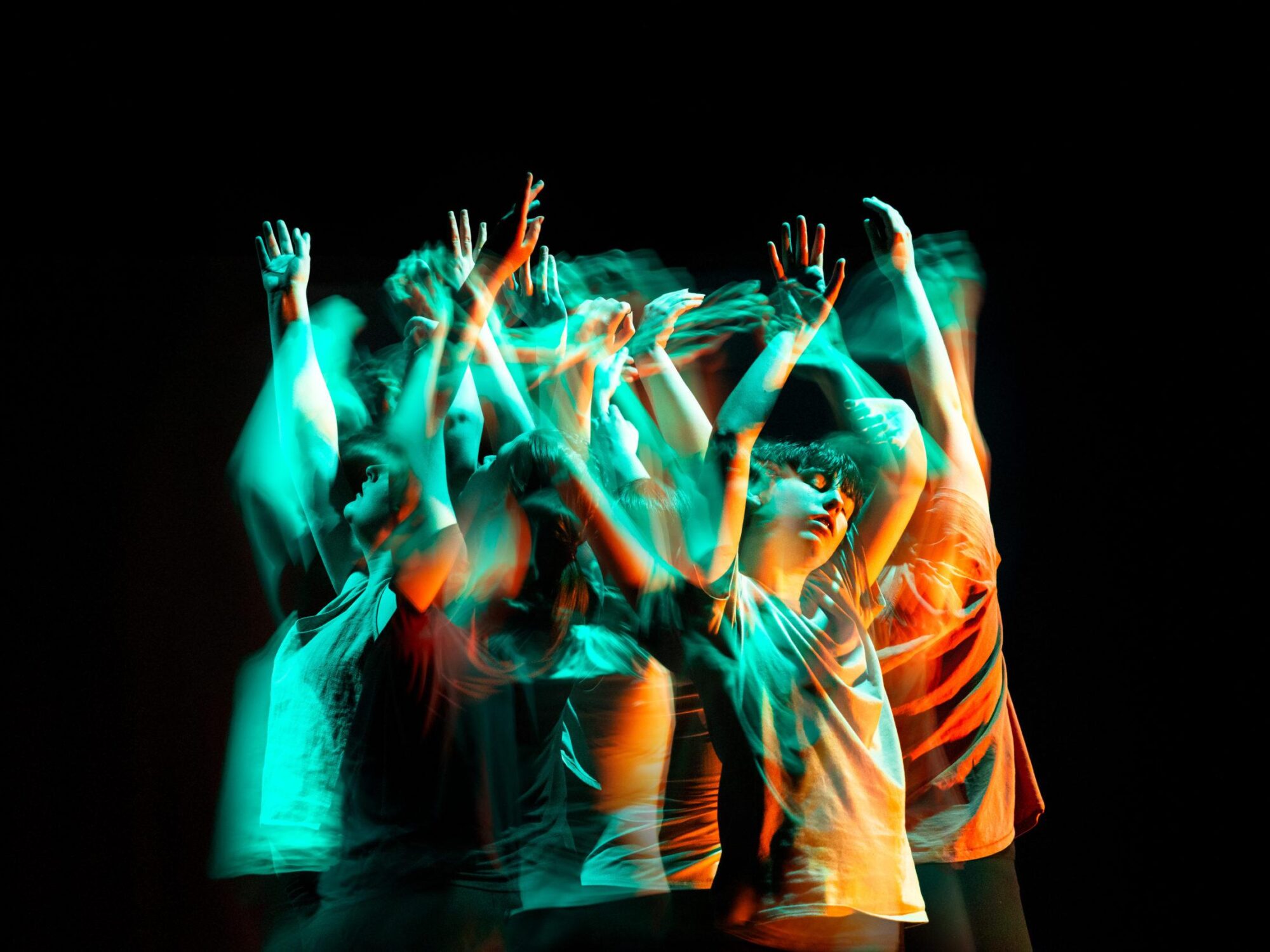 A group of dancers standing close together with their eyes closed and their arms in the air