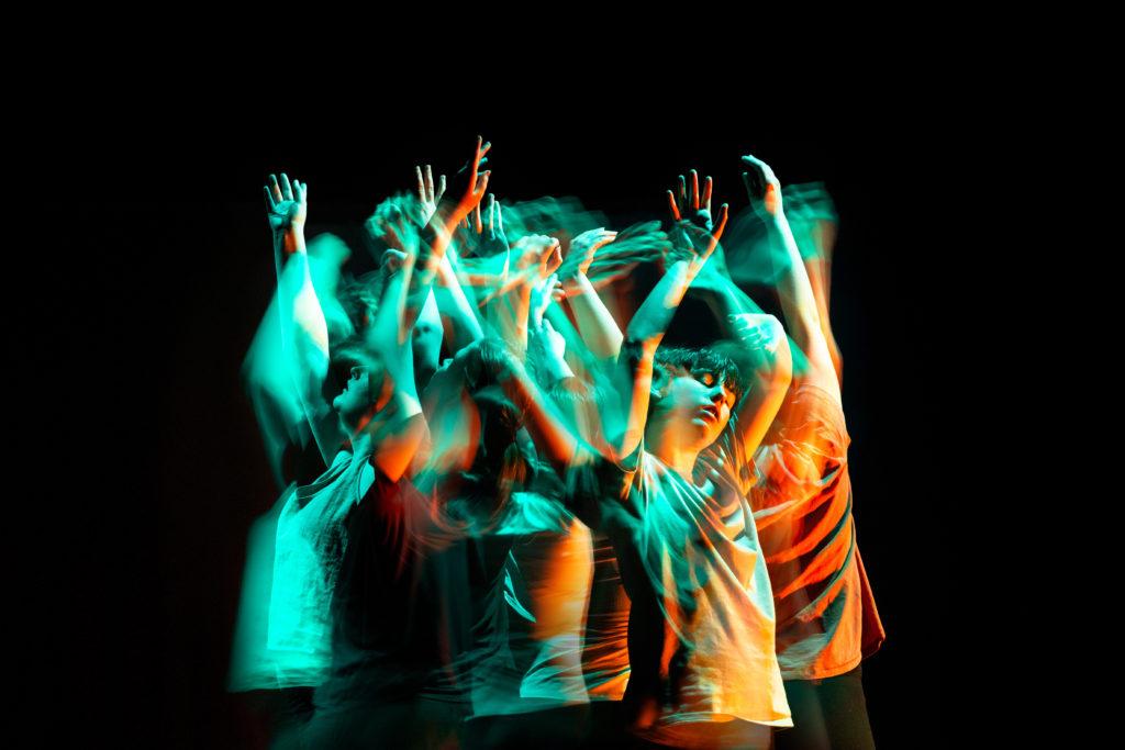 A group of dancers standing close together with their eyes closed and their arms in the air